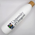 UofG Sugarcane Bottle. The bottle is white with the University of Glasgow crest printed vertically along the side, in full colour. It has a screw-top lid made of bamboo.