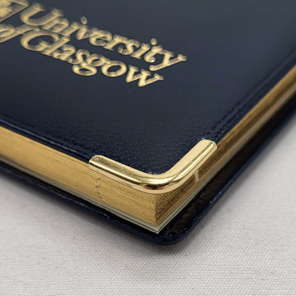 Pocket Diary 2026. Navy faux leather with gold embossed University of Glasgow logo on front, bottom edge. Gold corner protectors.