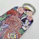Leather keyring featuring the Basket of Flowers textile design by Charles Rennie Mackintosh. The design depicts a stylised bouquet of brightly coloured flowers. The keyring is rectangular with a stainless steel loop at the top. The image shows a close-up of part of the keyring.