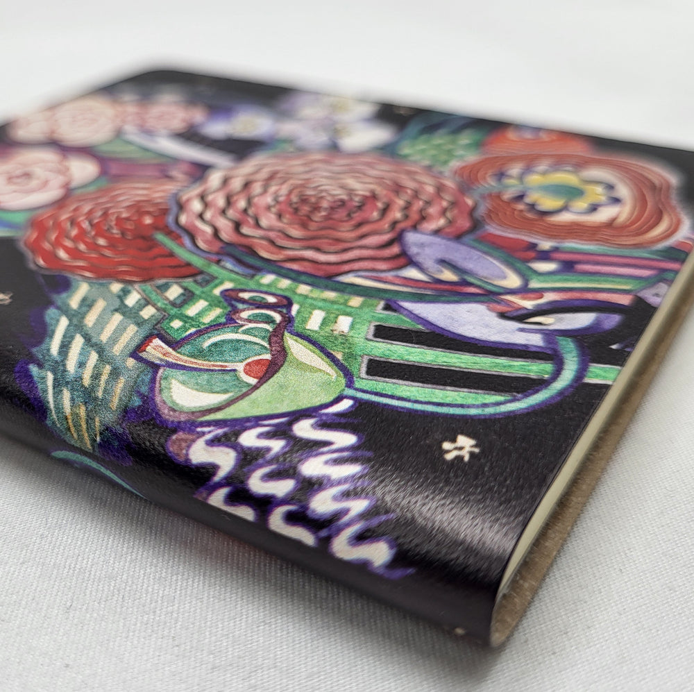 Notebook featuring the Basket of Flowers textile design by Charles Rennie Mackintosh. The design depicts a stylised bouquet of brightly coloured flowers. The image shows a close-up of the spine of the notebook.