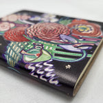 Notebook featuring the Basket of Flowers textile design by Charles Rennie Mackintosh. The design depicts a stylised bouquet of brightly coloured flowers. The image shows a close-up of the spine of the notebook.