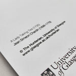 The image shows the reverse of the Lady Taking Tea greetings card. The reverse of the card is white with the title of the painting and the artist's name in black. The University of Glasgow Crest is also printed in black on the lower back corner.