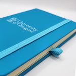 University of Glasgow Aqua A6 Pocket Notebook. The UofG crest is printed in white in the centre of the cover. The notebook has an aqua closure band.