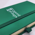 University of Glasgow Green A6 Pocket Notebook. The UofG crest is printed in white in the centre of the cover. The notebook has a green closure band.
