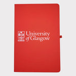 University of Glasgow Red A5 Notebook. The UofG crest is printed in white in the centre of the cover. The notebook has a red closure band and a red ribbon marker.