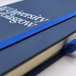 University of Glasgow Navy A5 Pocket Notebook. The UofG crest is printed in white in the centre of the cover. The notebook has a navy closure band and a navy ribbon marker.