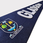 University Crest Pennant Flag (close up view). The image shows a close-up of the full-colour University of Glasgow crest, which is embroidered on the body of the pennant. The word 'GLASGOW' is stitched horizontally next to the crest in white felt. The pennant itself is navy blue felt.