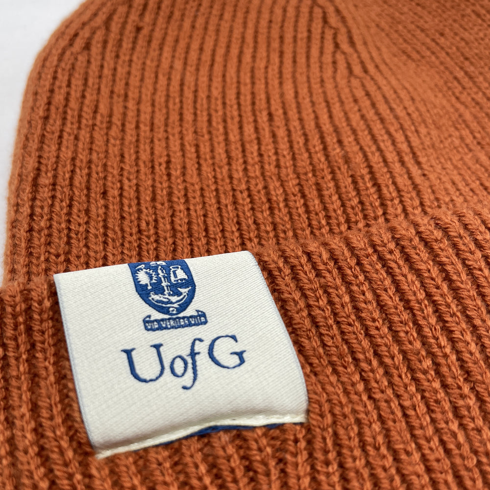 Brown knit beanie with a label featuring 'UofG' on a white background