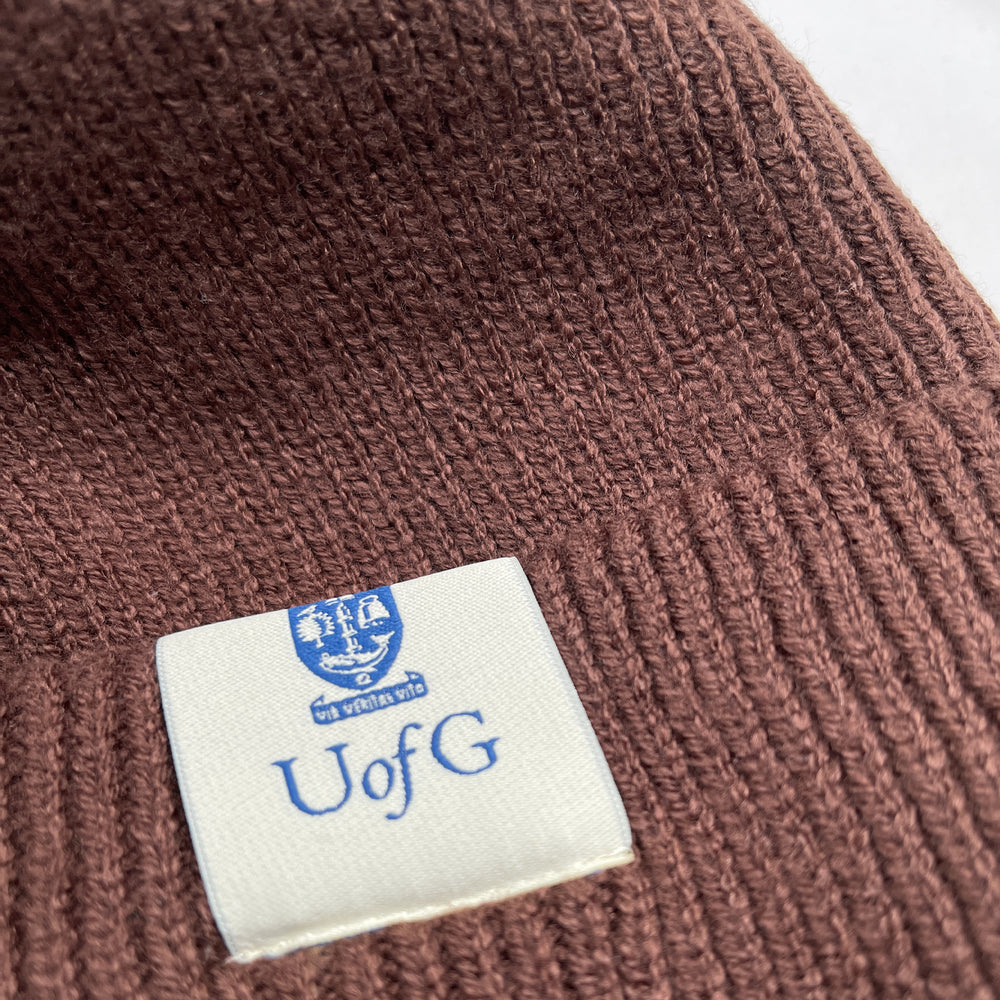 Brown knit beanie with a blue and white logo tag on a white background