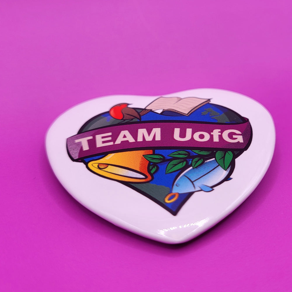 Heart-shaped button badge with 'TEAM UofG' text on a purple background