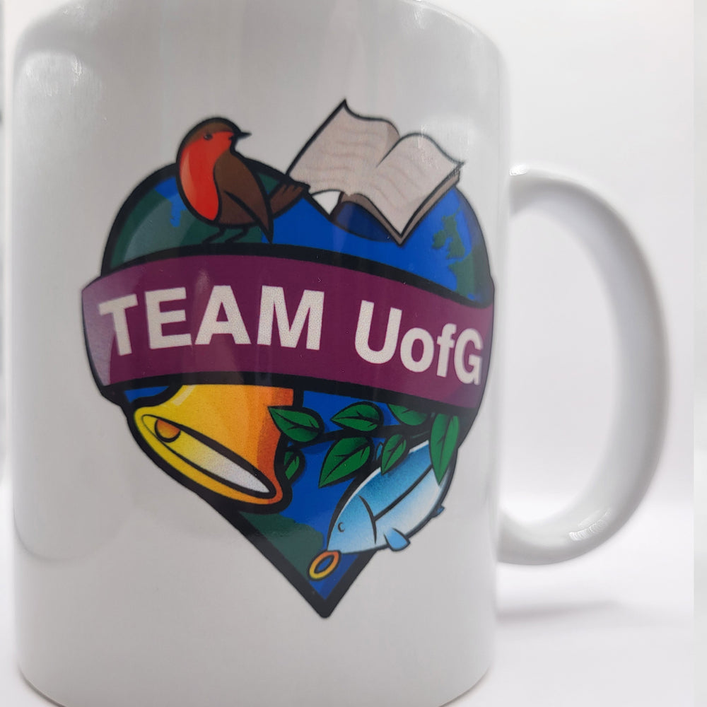 White mug with colorful 'TEAM UofG' logo featuring a bird, book, bell, and fish on a white background.