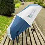 Umbrella with University of Glasgow logo on a wooden bench outdoors