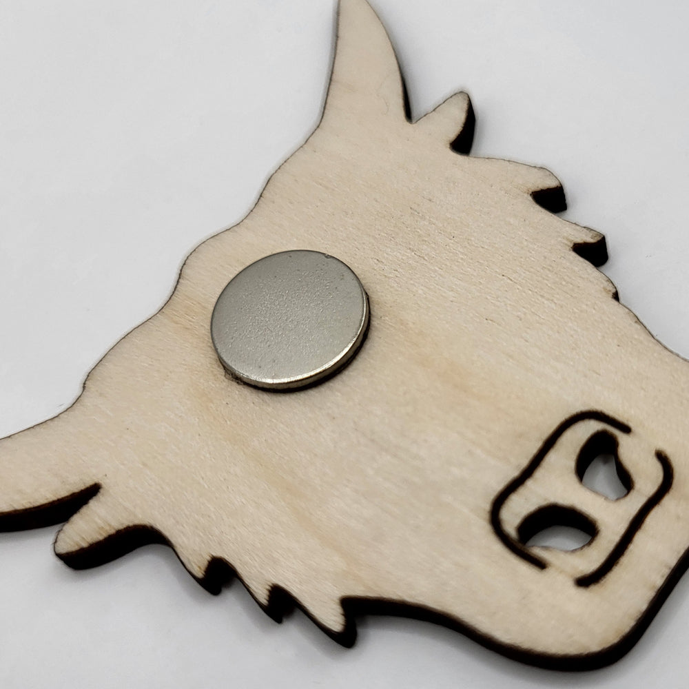 Wooden fridge magnet (reverse view). The magnet is in the shape of a highland cow's head. The reverse view shows the circular magnet and the unfinished surface of natural wood.