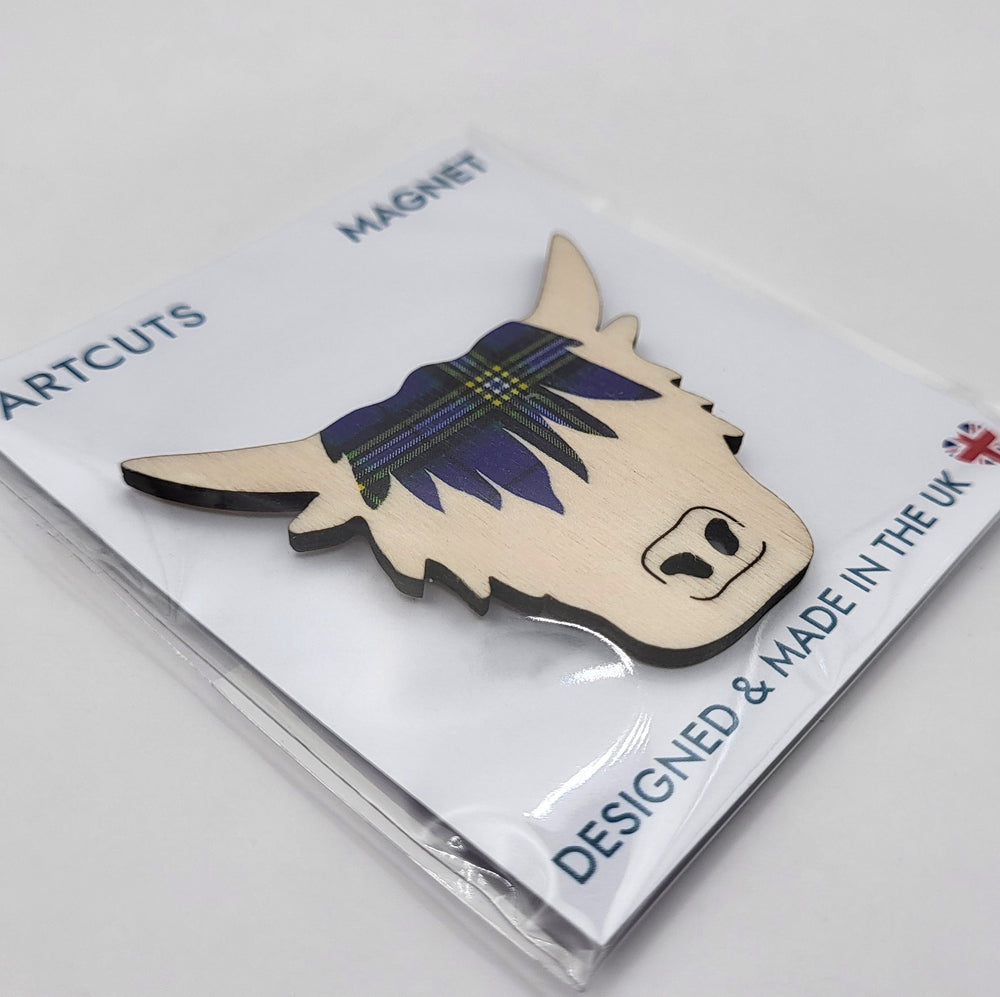 Wooden fridge magnet in packaging. The magnet is in the shape of a highland cow's head, with a fringe patterned with the University of Glasgow tartan. The packaging is a white backing card with a clear cellophane wrapping. The card reads: "Artcuts Magnet" along the top and "Designed and made in the UK" along the bottom.