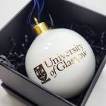 University of Glasgow Tree Bauble - White bauble with gold image of UofG logo. Inside black presentation box. Featuring a gold crown attachment and blue velvet ribbon. 