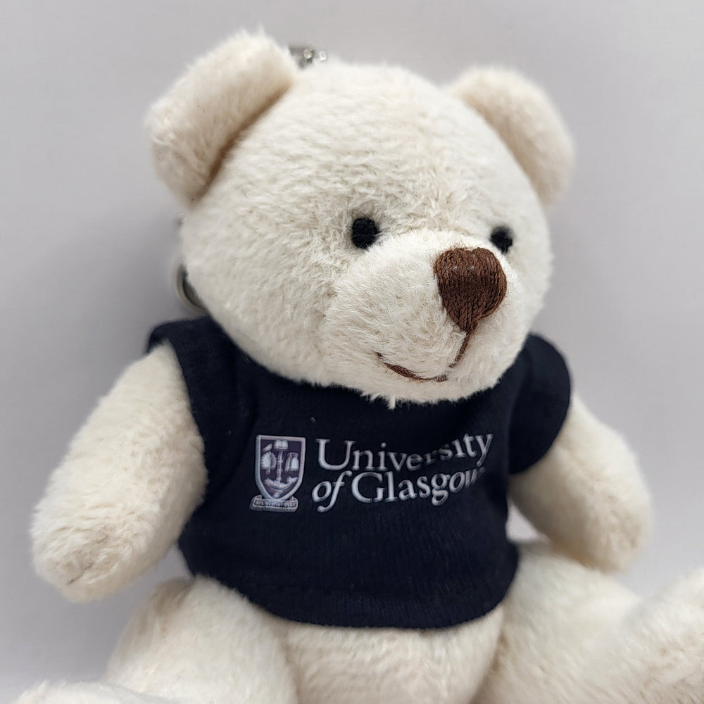 White teddy bear wearing a black 'University of Glasgow' shirt on a gray background