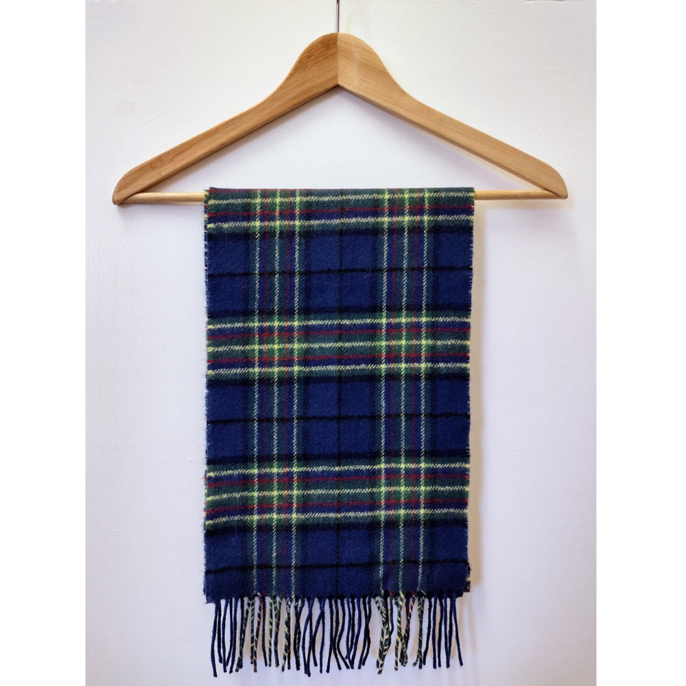 Wool scarf in the Adam Smith Business School tartan. The tartan is dark navy blue with a yellow, green and red pattern. It has woven tassels at each end. The image shows the scarf displayed on a wooden hanger.