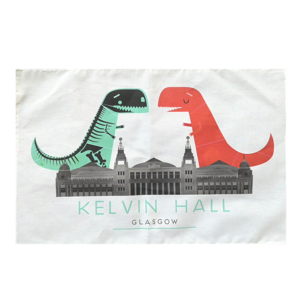Kelvin Hall Dino Tea Towel. A white cotton tea towel with a colour print in green, red and grey. The illustration shows a t-rex dinosaur facing a t-rex skeleton with the Kelvin Hall building below them. The text below the building reads "Kelvin Hall Glasgow" in block capitals.