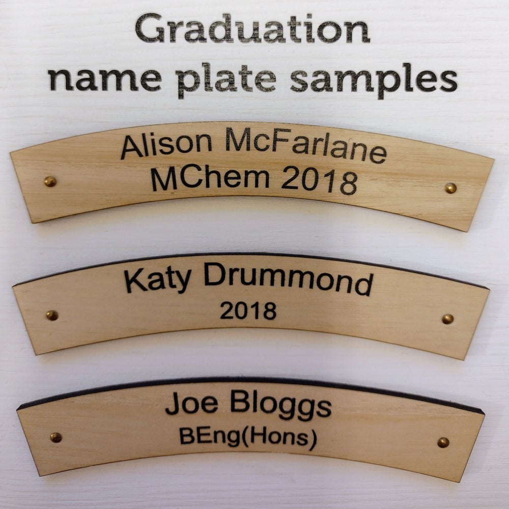 Three example nameplates for personalised University plaques. The example plates are made of light wood. Each have two lines of sample text on them. Each of the first lines is a sample student name, and each of the second lines is a qualification and/or graduating year.