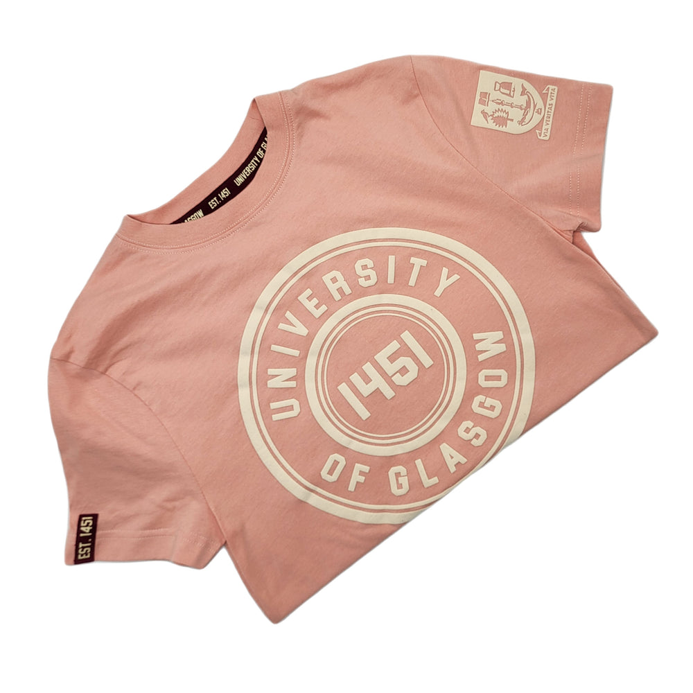 University of Glasgow Organic Cotton Circle T-Shirt in salmon pink. The image shows the t-shirt folded in half. There is an off-white circle design printed on the chest. The UofG crest is printed in off-white on the sleeve. The circle design consists of the words "University of Glasgow" in block capitals, with the date 1451 in the middle. 