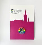 University of Glasgow Pride Pin Badge on backing card. A rainbow enamel pin badge in full colour with the University of Glasgow crest in the centre. The badge is shown displayed on a magenta and white backing card.